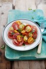 Повышенный вид томатного салата с тремя различными видами помидоров, украшенный базиликом — стоковое фото