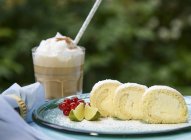 Daytime view of lemon Roulade with lime wedges, red currants and iced coffee — Stock Photo
