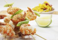 Crispy fried crayfish skewers with lime and grated coconut over white surface — Stock Photo