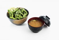 Miso soup and salted soya beans in bowls on white background — Stock Photo