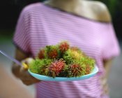 Frau hält Teller mit Rambutanen — Stockfoto