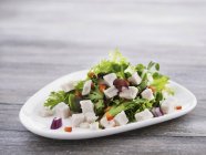 Fresh mixed leaf salad with chicken, onions and peppers on white plate over wooden surface — Stock Photo