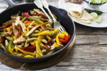 Chicken fajita with peppers in black frying pan over wooden surface — Stock Photo