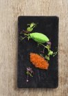 Vue de dessus des oeufs de poisson orange et vert avec des herbes sur le tableau noir — Photo de stock