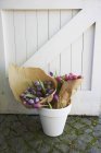 Tulipani rosa e viola avvolti in carta in un vaso da fiori bianco vicino al cancello di legno — Foto stock