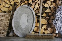 Una vieja escoba y una bandeja de metal en un banco de madera frente a una pila de madera - foto de stock