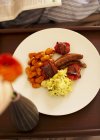 An English breakfast with scrambled eggs, baked beans, tomatoes, bacon and sausages on white plate — Stock Photo