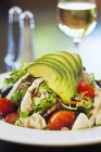 Cobb salad with avocado, tomatoes, bacon and chicken served with a glass of wine — Stock Photo