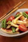 Fried vegetables in a bowl with chopsticks over plate — Stock Photo