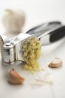 Garlic in a crusher over white surface — Stock Photo