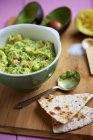Guacamole with ingredients on wooden surface with bowl and spoon — Stock Photo
