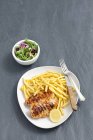 Сверху вид жареной курицы с картошкой фри, ломтиком лимона и овощным салатом — стоковое фото