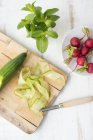 Cucumber on chopping board with radishes — Stock Photo