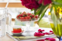 Closeup view of fresh strawberries in glass dish and mocha cup on book with rose petals — Stock Photo