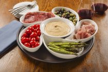 Trempette au houmous avec jambon, salami, olives et légumes dans des bols — Photo de stock