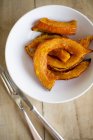 Baked Hokkaido pumpkin wedges on white plate over wooden surface with fork — Stock Photo