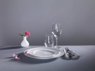Un luogo con piatti, posate, bicchieri vuoti e un vaso di fiori su sfondo grigio — Foto stock