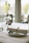 Un tovagliolo di tessuto su un piatto e bicchieri vuoti su un tavolo in un ristorante — Foto stock