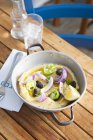 Картофельное пюре с луком и оливками в горшке за столом — стоковое фото