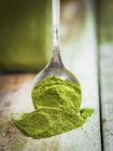 Moringa polvere verde su un cucchiaio e una superficie di legno — Foto stock