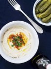Hummus and gherkins on white plates over black surface — Stock Photo