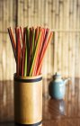Vista close-up de pauzinhos coloridos em um recipiente de bambu em uma mesa de madeira — Fotografia de Stock