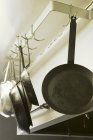 Closeup view of metal frying pans hanging on hooks in kitchen — Stock Photo
