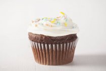 Cupcake with white frosting and sugar sprinkles — Stock Photo