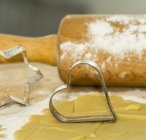 Closeup view of cookie cutters with rolling pin and biscuit pastry — Stock Photo