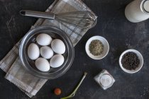 Huevos, especias, cebolla de primavera, tomates cherry y batidor en la superficie negra - foto de stock