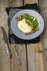 Картопляне пюре з масляним горохом і нарізане тофу на сірій тарілці над дерев'яною поверхнею з виделкою та ножем — стокове фото