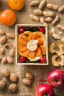 Dried fruits, nuts and fresh fruit in wooden crate over textile surface — Stock Photo