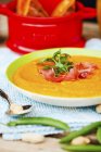Pumpkin soup with bacon and herbs on white plate over towel with spoon — Stock Photo