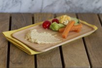 Un plato de hummus y verduras en bandeja de madera sobre mesa de madera - foto de stock