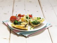 Two slices of potato tortilla with broccoli on white plate over towel on wooden surface — Stock Photo
