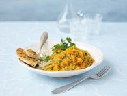 Curry de lentejas vegetarianas en placa blanca sobre superficie azul con tenedor - foto de stock