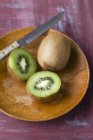 Kiwi with halves on wooden plate — Stock Photo