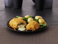 Garlic chicken kiev with mange tout and potatoes on black plate — Stock Photo