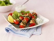 Greek chicken, pepper and courgette kebabs with salad  on white plate over towel — Stock Photo