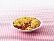Closeup view of rhubarb Crumble in bowl on checkered cloth — Stock Photo