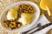Eggs Benedict with fried potatoes and mushrooms in white plate — Stock Photo