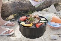 Vista diurna di carne e verdure su barbecue con gambe umane sullo sfondo — Foto stock