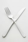 Closeup view of crossed knife and fork on white surface — Stock Photo