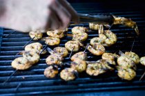 Closeup cropped view of hand arranging prawn skewers on barbecue rack — Stock Photo