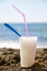 Closeup view of Granita in beaker with straw and spoon on sandy beach — Stock Photo