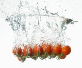 Tomates cherry cayendo en el agua - foto de stock
