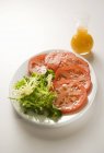 Tomates en rodajas con verduras; Aderezo de ensalada en plato blanco - foto de stock