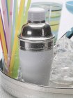 Closeup view of cocktail shaker with ice cubes, glasses and straws — Stock Photo