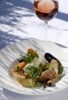 Рыба и моллюски с овощами на белой тарелке, бокал вина — стоковое фото