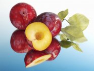 Red plums with half and leaves — Stock Photo